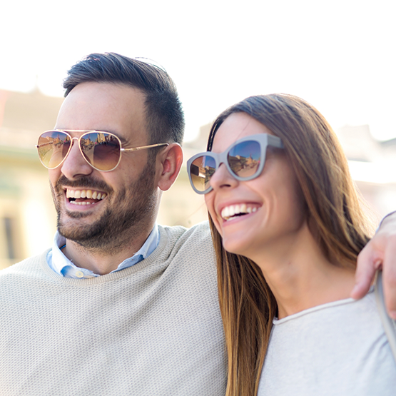 Young man and woman smiling outdoors with sunglasses